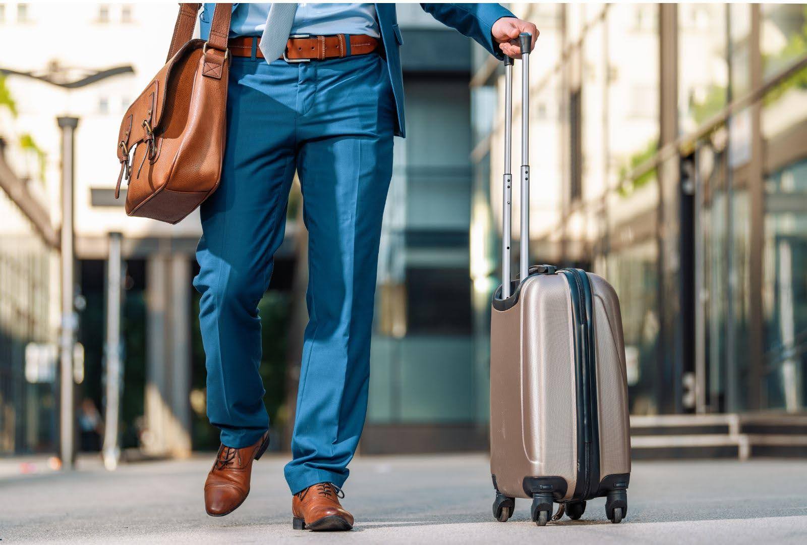 Business traveller walking with a wheeled suitcase and carrying a leather messenger bag, showcasing ergonomic travel gear for comfort and ease.